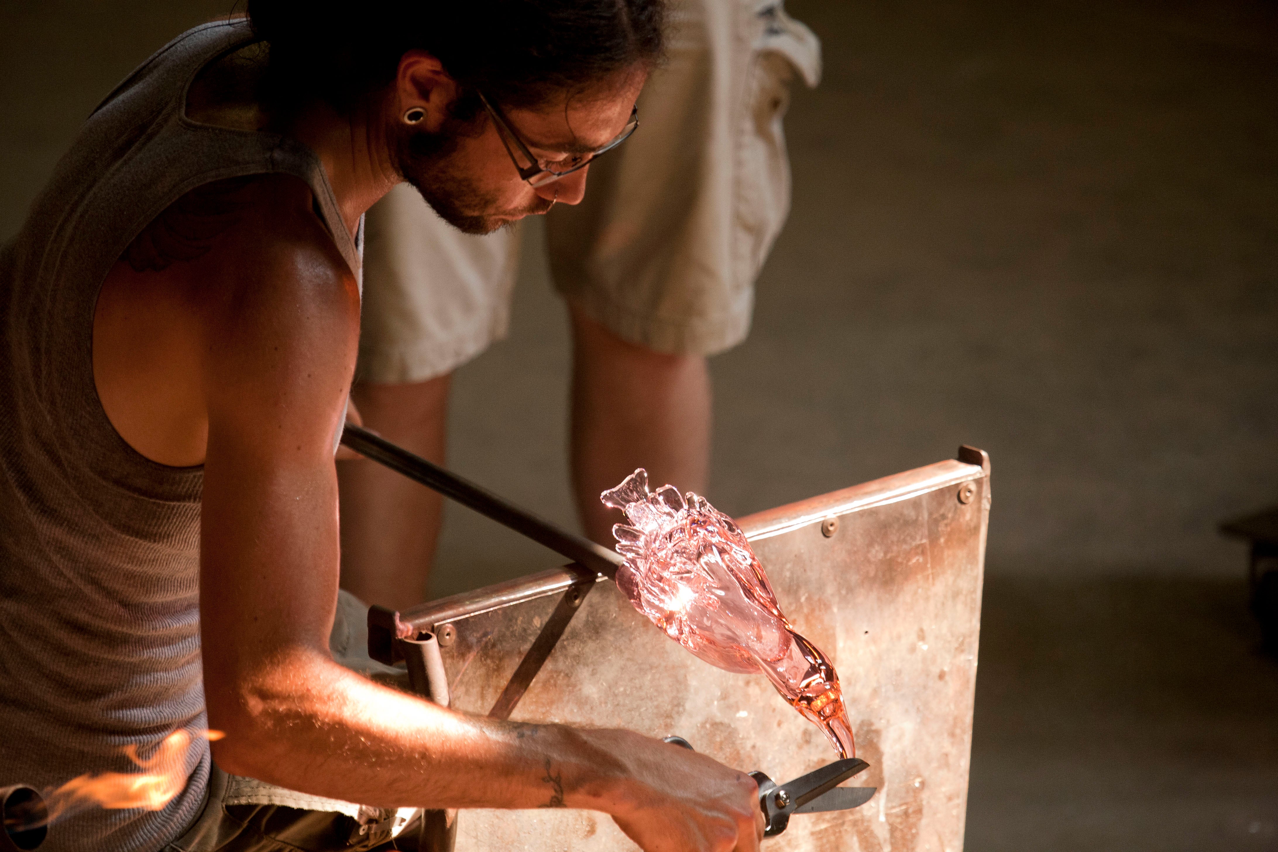 A glassmaker shaping hot glass with hand tools at Wheaton Village