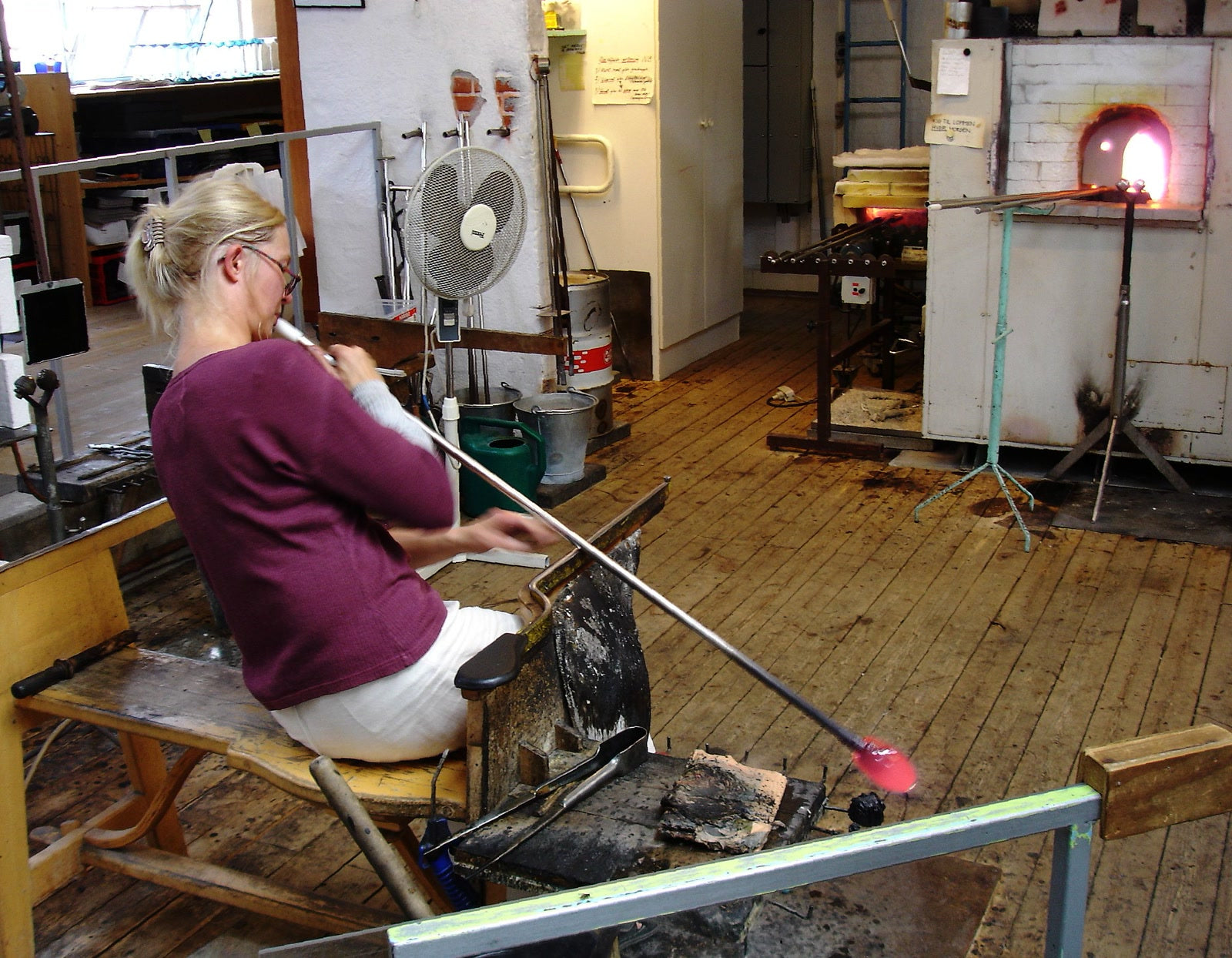 A glassmaker blowing through a blowpipe into hot glass
